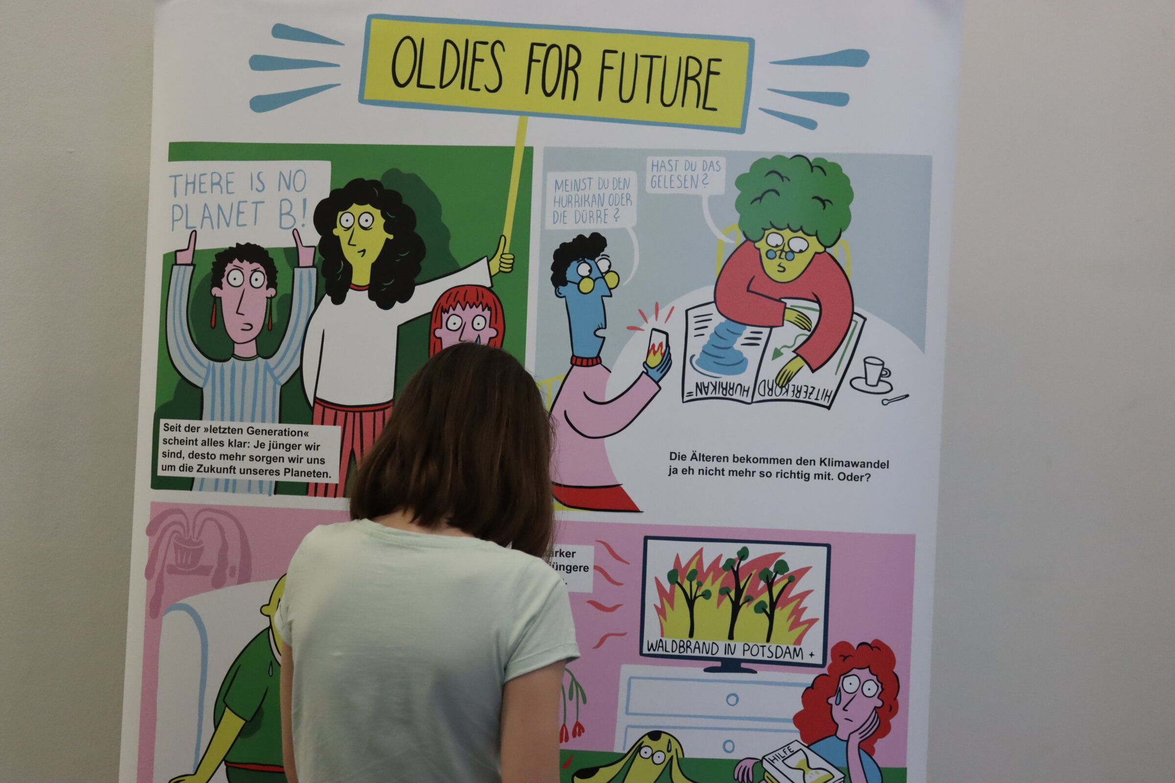 Eine Frau steht vor einem Rollup mit dem Comic &bdquo;Oldies for Future&ldquo;. Zu erkennen sind drei Bilder des Comics, in denen es darum geht, dass sich &auml;ltere Menschen Sorgen um die Folgen des Klimawandels machen.