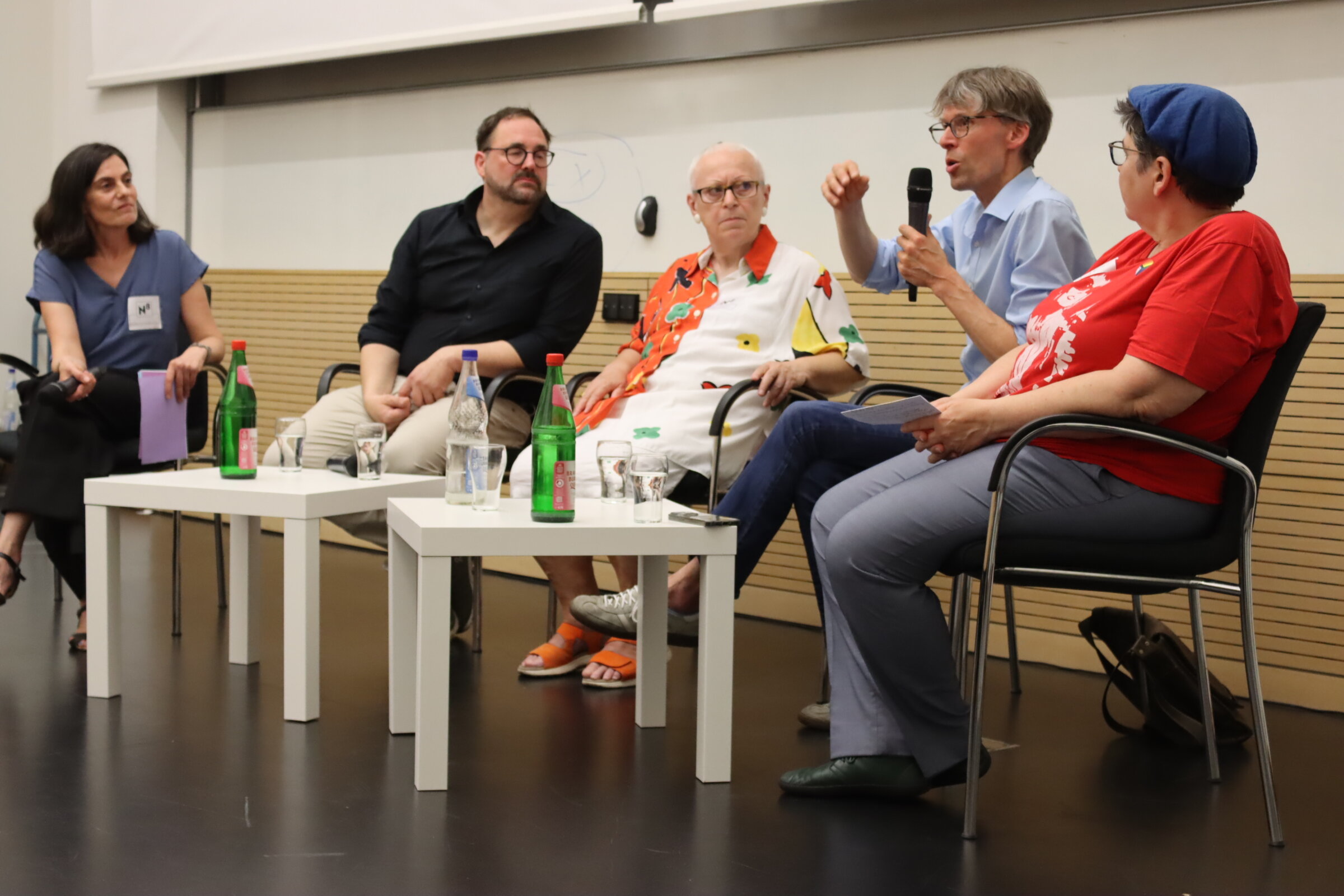 Das Foto zeigt die genannten Personen auf dem Podium sitzen und miteinander sprechend.