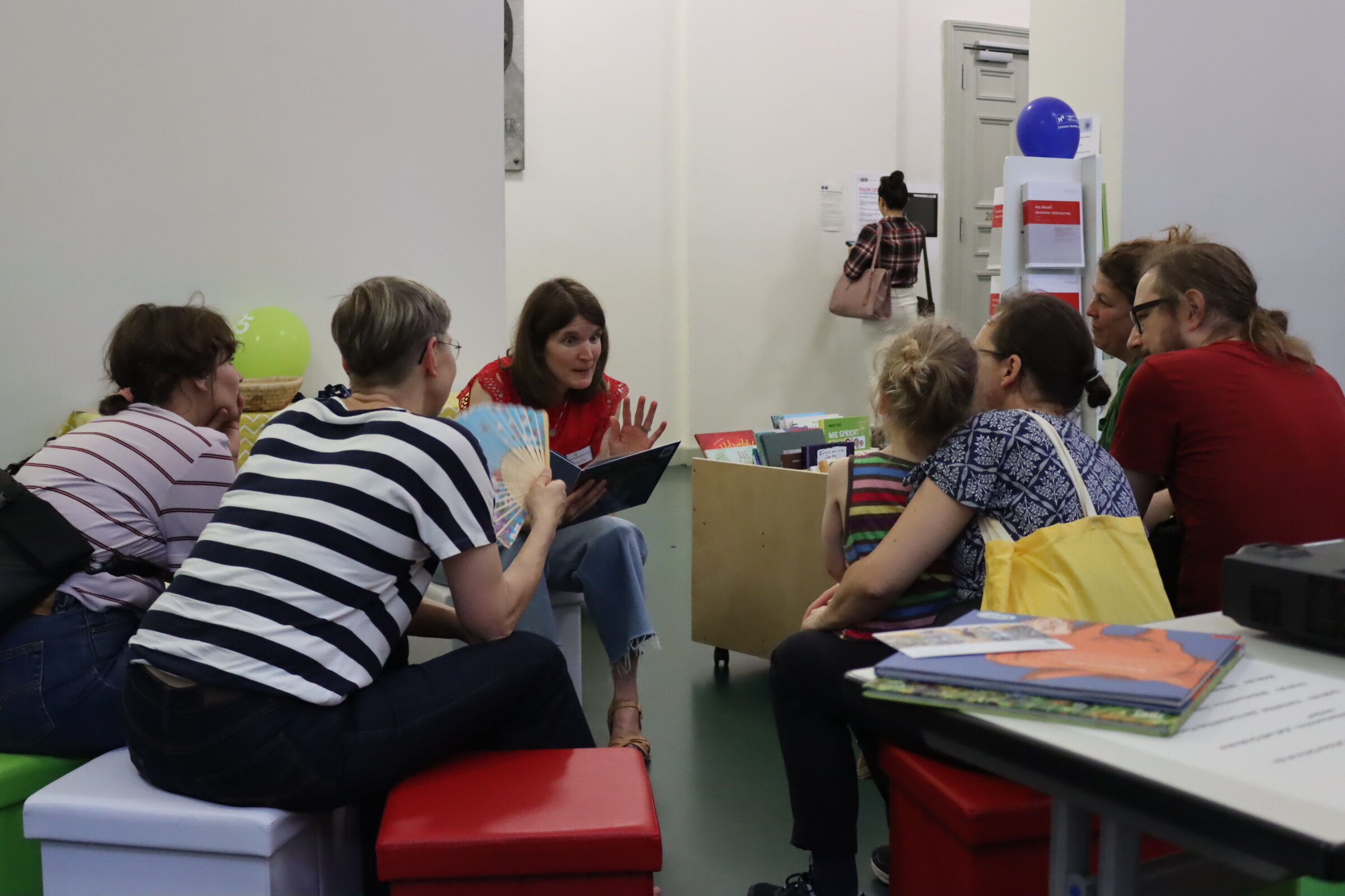 Das Foto zeigt eine Mitarbeiterin der kooperierenden Bibliothek, die einer kleinen Gruppe von Kindern und Erwachsenen vorliest.